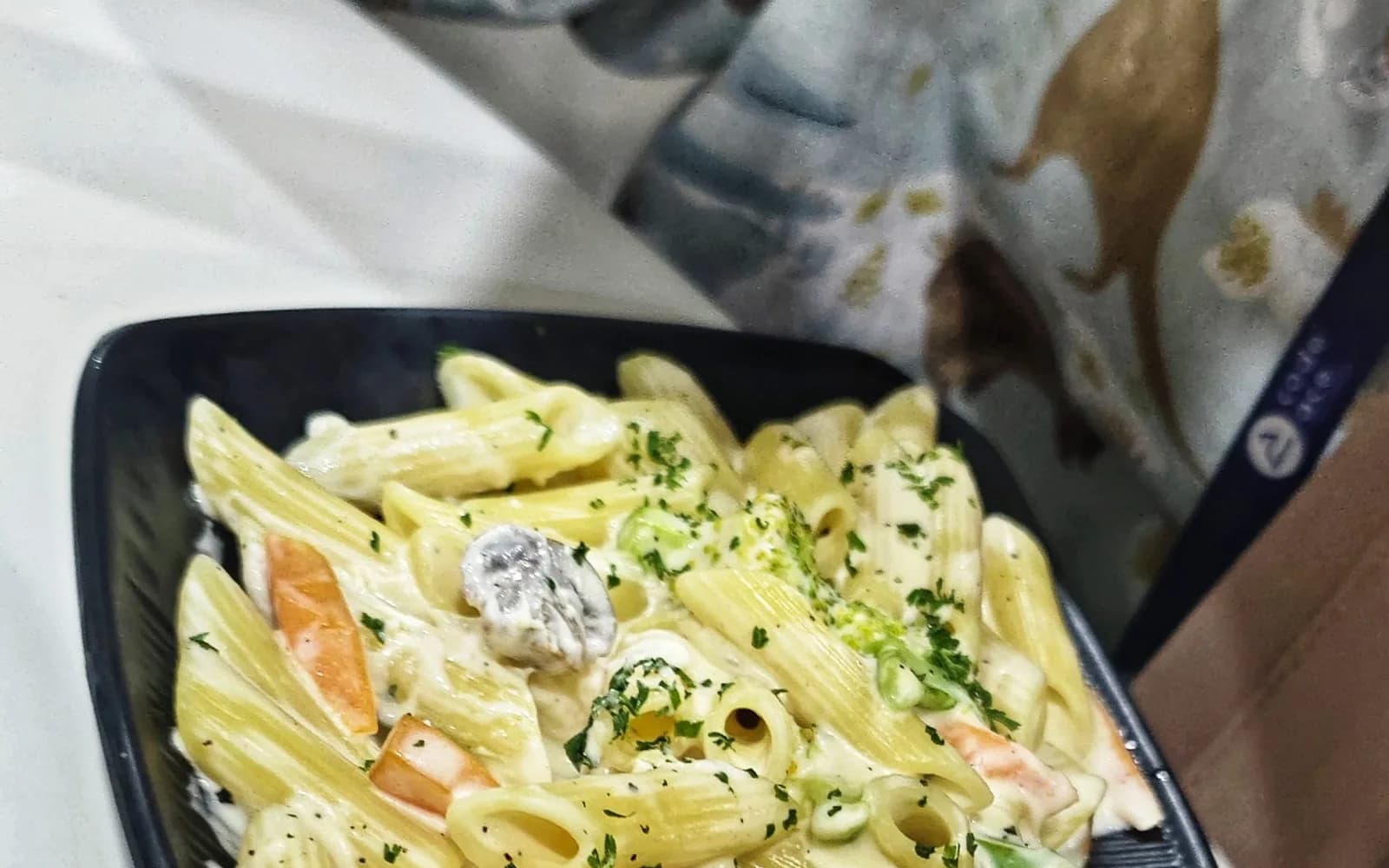 Penne pasta in a creamy sauce served in a dark bowl