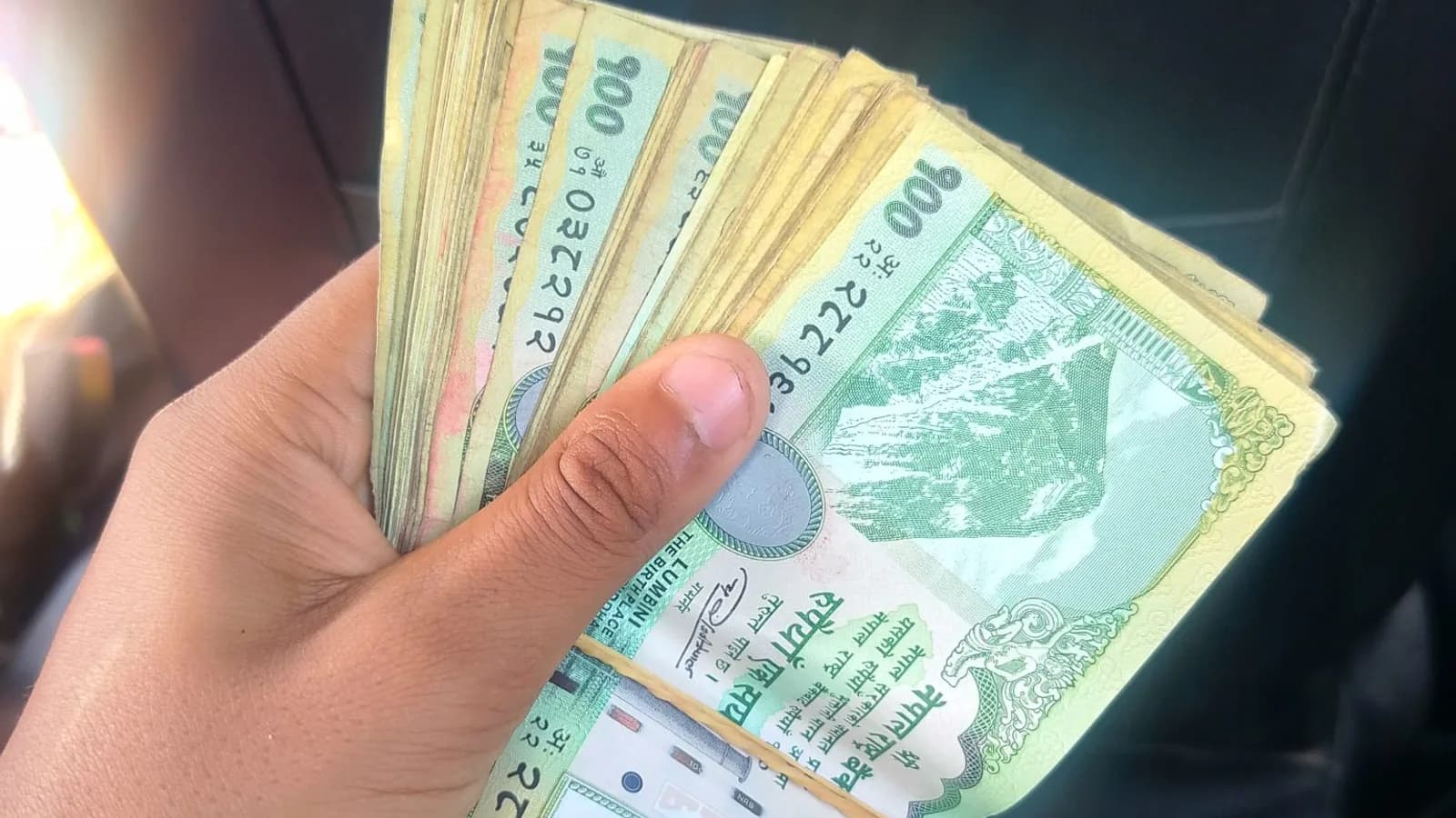 A hand holding a fanned stack of banknotes