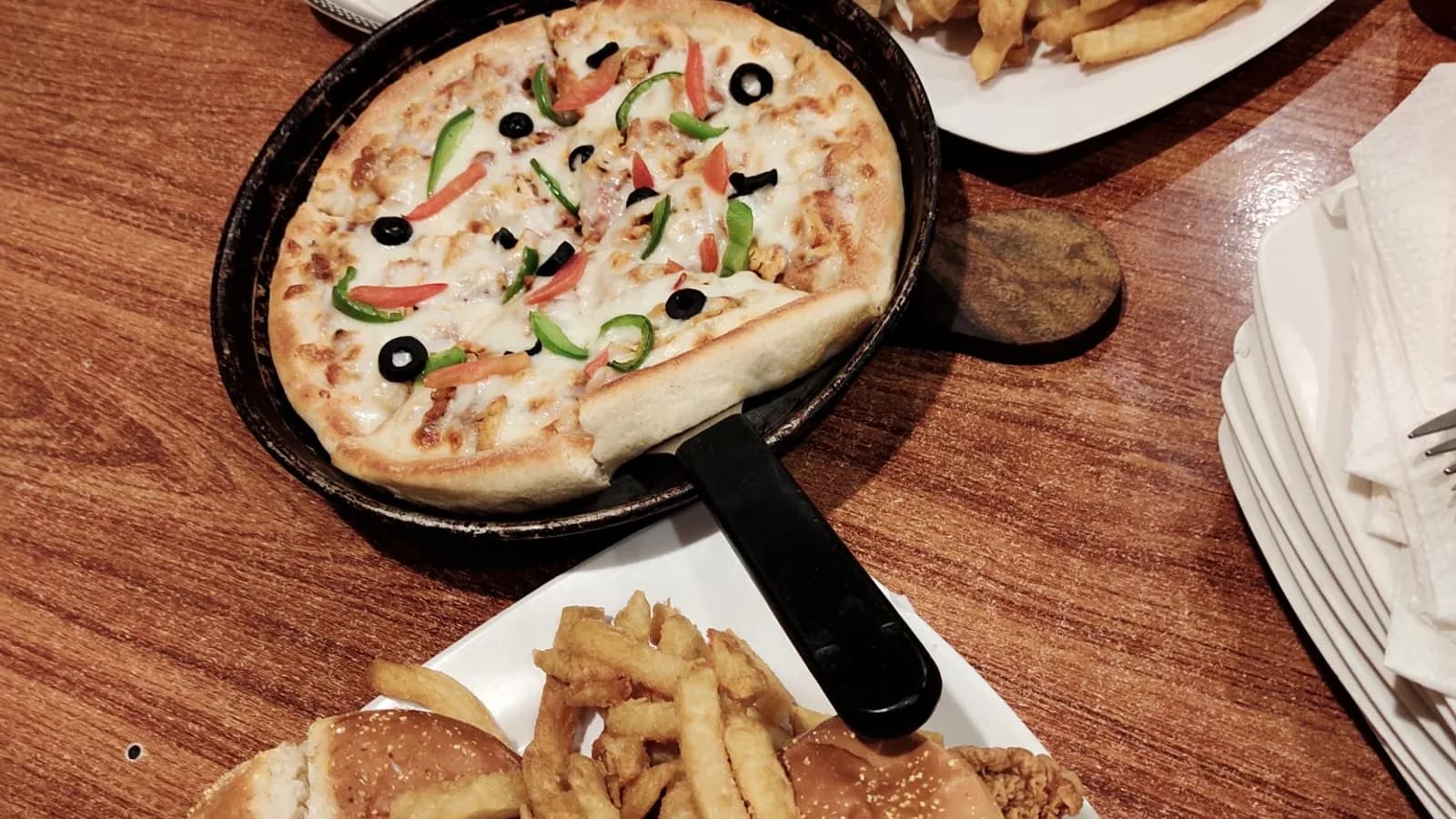 A pizza in a pan on a wooden table set with several plates of food