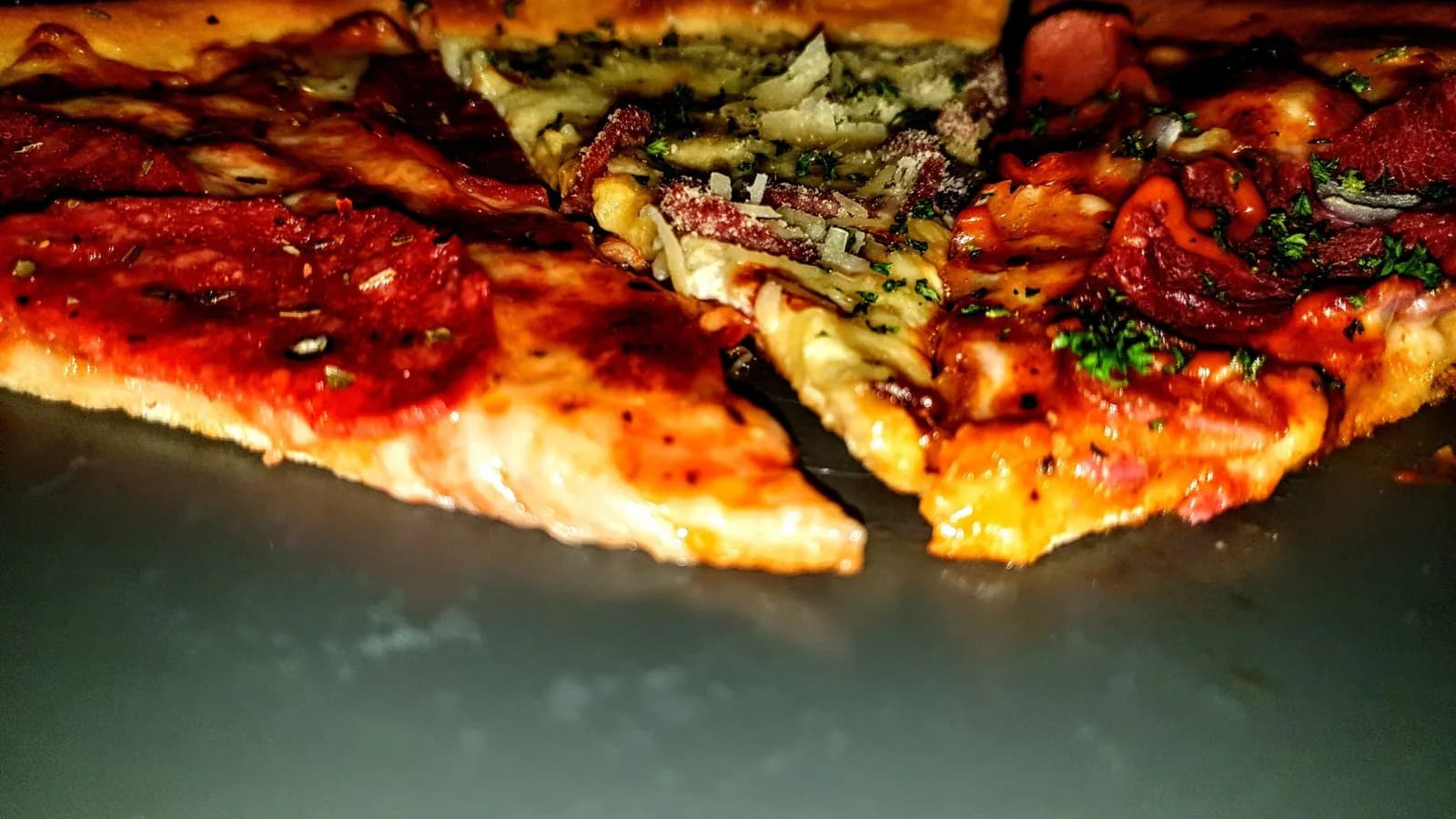 Three pizza slices photographed close up on a dark background