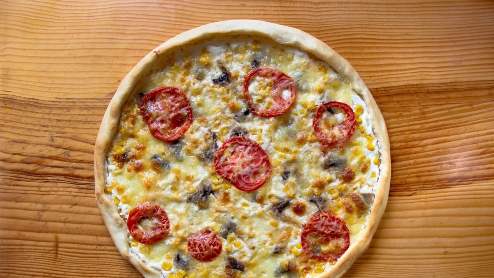 Round pizza topped with tomato and olives on a wooden board